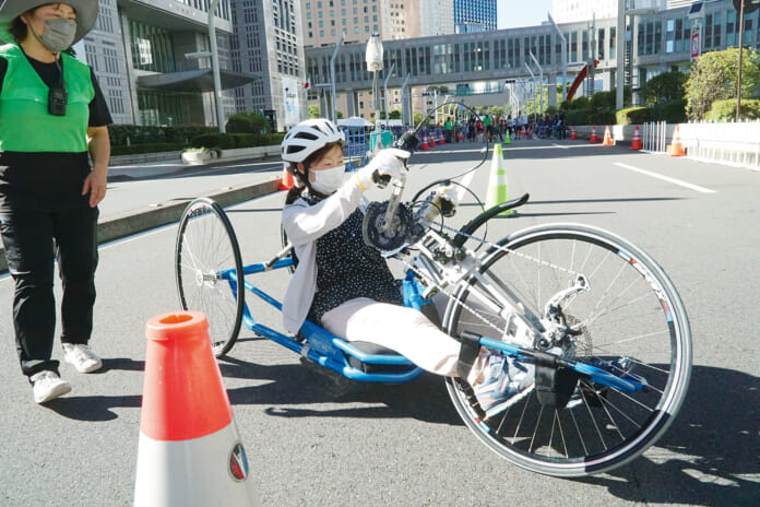 仰向けに近い状態で腕を使い車輪を回す「ハンドサイクル」＝８月24日午後、東京都庁前